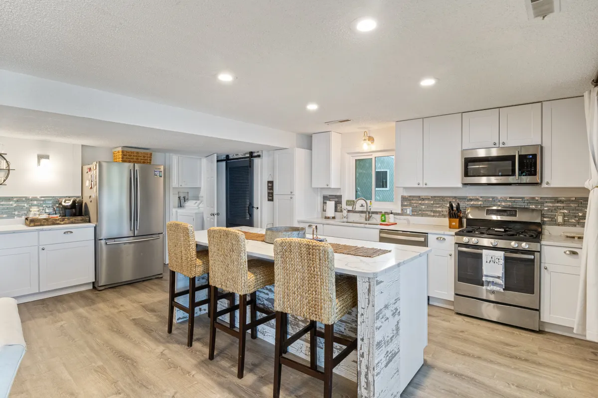A modern kitchen with a central island outfitted with bar stools, sleek stainless steel appliances, modern cabinetry, and a decorative backsplash. The space is bright and designed for both cooking and gathering, inviting guests to participate in meal prep or enjoy a casual breakfast at the island.