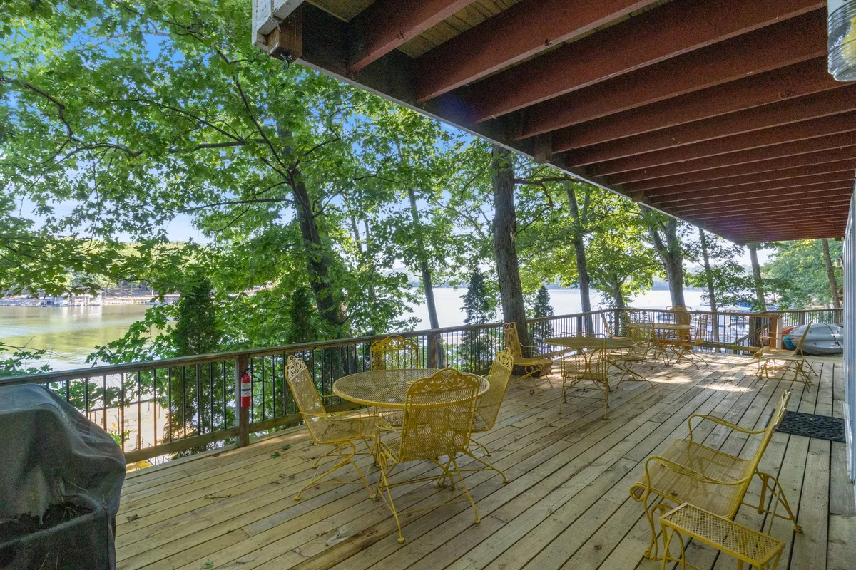 A welcoming wooden deck with yellow metal furniture overlooks lush green trees and offers a distant view of the water. The deck invites relaxation, outdoor dining, and quiet moments while staying close to nature.