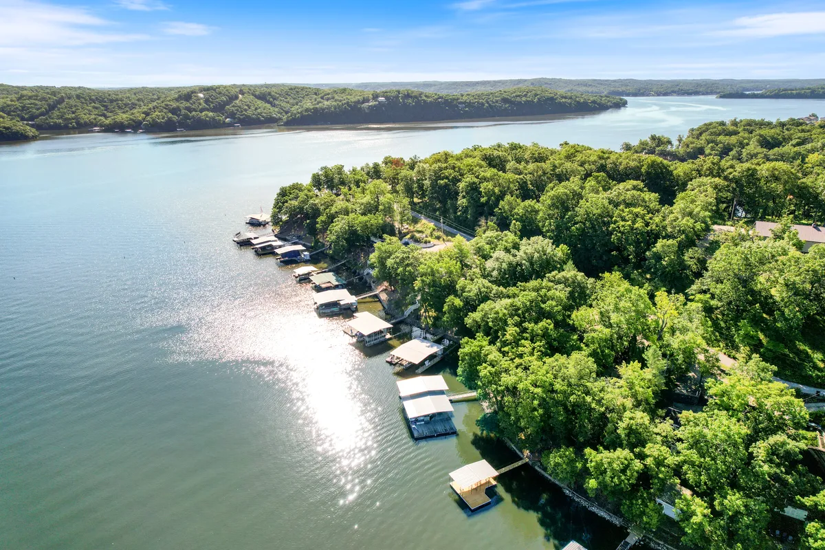 A sweeping view of the lake framed by docks, green trees, and distant hills. The wide perspective emphasizes the natural beauty and recreational opportunities, showcasing a setting perfect for boating, fishing, and observing the annual boat race or air show from afar.