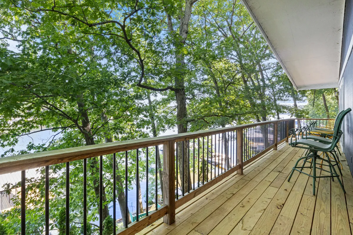 A wooden deck surrounded by green trees, with metal chairs facing a panoramic lake view. The deck is spacious and inviting, perfect for group gatherings, sunrise coffees, or evening relaxation under the stars.