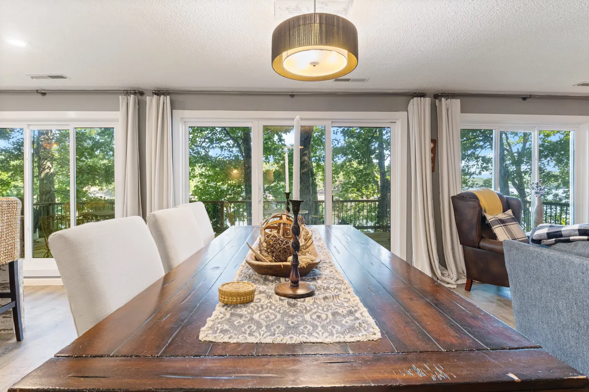 A cozy dining and living space with a prominent wooden table set near large windows, ambient decorative items, and comfortable seating. Sunlight floods the area, creating a warm and inviting environment perfect for group meals or game nights.